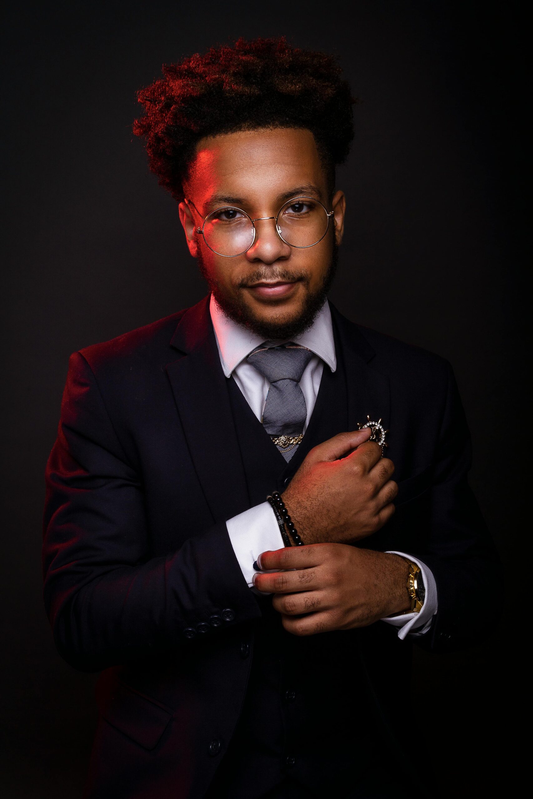 Portrait of a stylish young man in a dark suit with eyeglasses, exuding confidence.